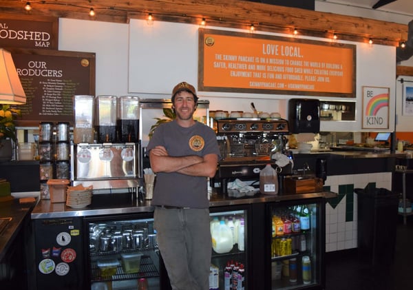 Benjy Photo leaning on counter with logo on shirt